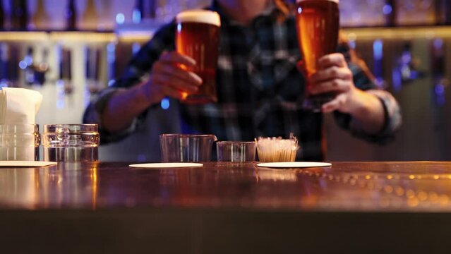 Young man, bartender serving two glasses of chill lager beer at bar, pub. Unfocused image of man smiling. Concept of alcohol drink, party, taste, relaxation, brewery. Ad