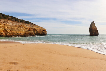 Cliff extending into ocean with a rock on a sandy beach along the Seven Hanging Valleys Trail on a sunny winter day in southern Portugal.