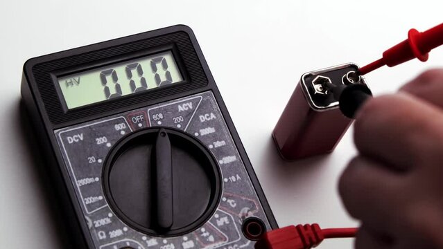 Checking the battery for 9 volts. The hand holds the probes of a multimeter and a nine-volt battery.