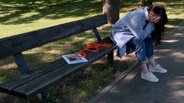 Heartbroken dog owner mourns as she sits on a bench with a dog collar and a missing dog notice. Pet relatives and love concept.