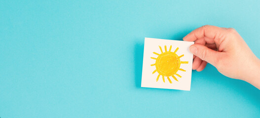 Holding a paper with a yellow sun, hot temperture on a summer day, positive attitude and hope,...