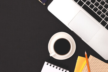 Office supplies, laptop and cup of coffee on a black background. Business workspace with copy space.