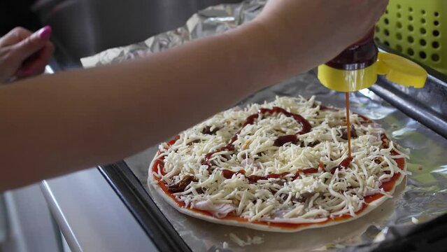 Video of a young woman's hand drawing a heart with barbecue sauce on the dough with tomato to prepare a homemade pizza.