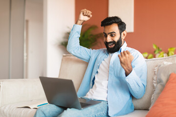 Joyful Middle Eastern Man Using Laptop Shaking Raised Fists Indoor