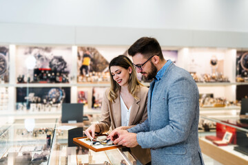Elegant middle age businessman choosing and buying his new expensive watch. Beautiful young female seller helps him to make good decision. Fashion style and elegance concept. - obrazy, fototapety, plakaty