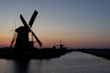 Naklejka premium Beautiful wooden windmills at sunset in the Dutch village of Kinderdijk. Windmills run on the wind. The beautiful Dutch canals are filled with water. Beautiful sunset.