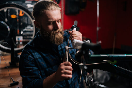 Closeup side view of serious bearded repairman checking and repairing bicycle handlebar with special tools working in bike repair shop with dark interior. Concept of professional maintenance of bike. © dikushin