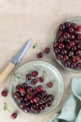 Plate of fresh red cherries and knife on beige background. Top view. Copy space.