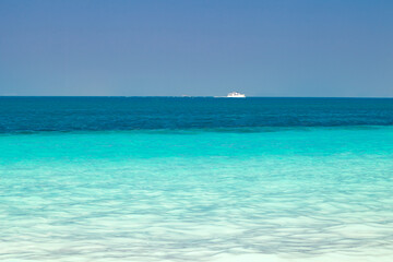 Fototapeta na wymiar Sea, turquoise clear water, white boat floating in distance