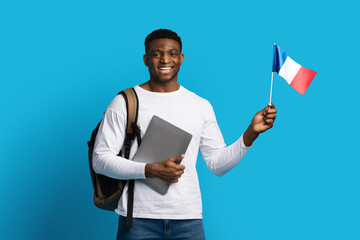 Cheerful young black man holding laptop and flag of France