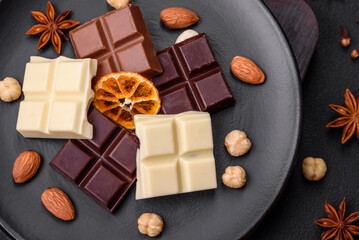 A mix of several types of delicious sweet chocolate broken into cubes on a black plate