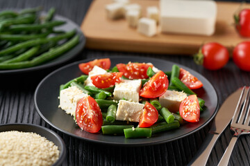 greek green beans and  tomato, herbs and olive oil on white plate served with feta cheese.