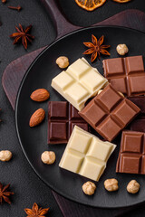 A mix of several types of delicious sweet chocolate broken into cubes on a black plate