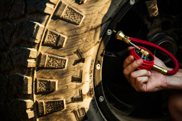 A man's hand checking the pressure on a 4x4 tire with a red gauge