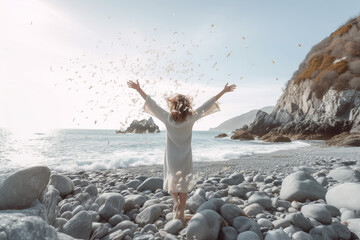 Woman with outstretched arms enjoying the wind and breathing fresh air on the rocky beach - obrazy, fototapety, plakaty