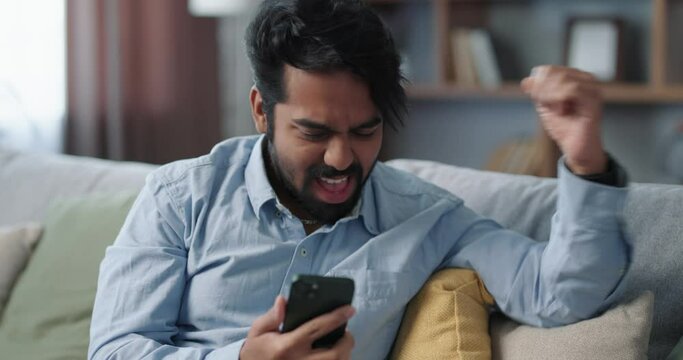 Overjoyed Indian young man sitting on the sofa finds out he won the lottery. 
