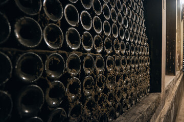 Stacked aged wine bottles covered with cobweb. Wine bottles in a bodega. Wine cellar in a cave. Bottles on a winery shelf covered by soft black mold