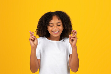 Cheerful curly teenager black schoolgirl in white t-shirt crossed fingers, make wish