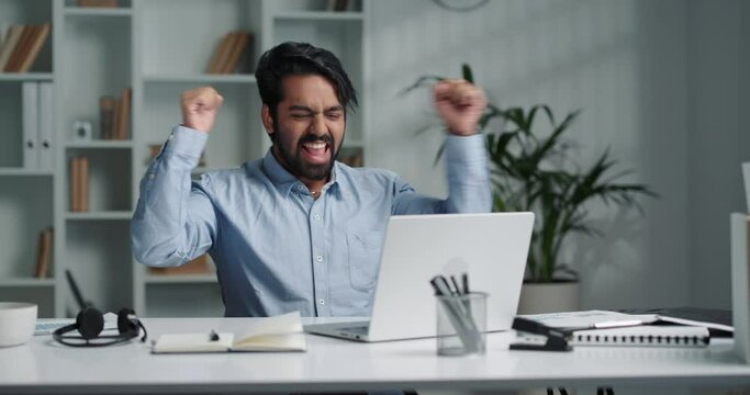 Cheerful Indian man receives a message about a lottery win on a laptop. 