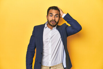 Professional young Latino man in business suit, yellow studio background, being shocked, she has remembered important meeting.