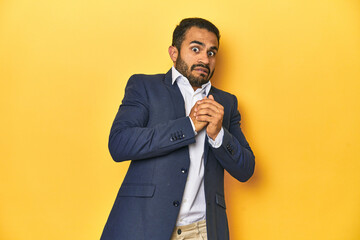 Professional young Latino man in business suit, yellow studio background, scared and afraid.