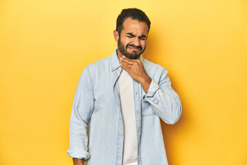 Casual young Latino man against a vibrant yellow studio background, suffers pain in throat due a...