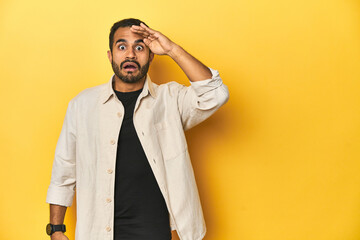 Fototapeta premium Casual young Latino man against a vibrant yellow studio background, shouts loud, keeps eyes opened and hands tense.