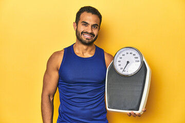 Fit Latino athlete holding a scale, focused on fitness and health goals.