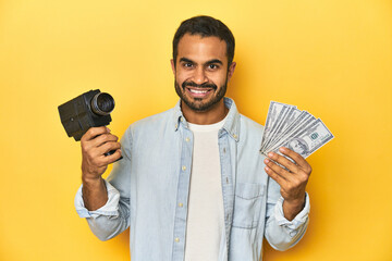 Young Latino man with vintage video camera and money, earning from filmmaking.