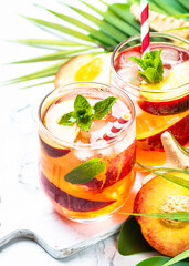 Peach cocktail, iced peach tea, fruit drink, summer beverage with fresh fruits, ice and mint. Close up.