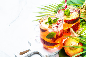 Peach cocktail, iced peach tea, fruit drink with palm leaves at tropical background.