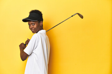 African woman golfer preparing to swing at ball, yellow studio background.
