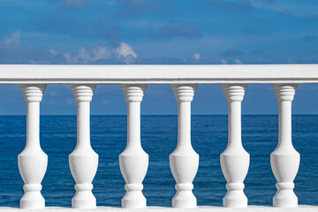 White railings with balusters on embankment against background of blue sea and sky, selective focus