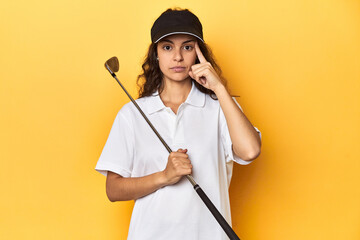Golfer woman with cap, golf polo, yellow studio, pointing temple with finger, thinking, focused on a task.
