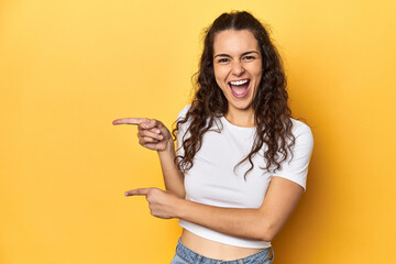 Young Caucasian woman, yellow studio background, pointing with forefingers to a copy space, expressing excitement and desire.