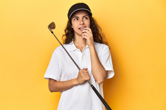 Golfer woman with cap, golf polo, yellow studio, relaxed thinking about something looking at a copy space.
