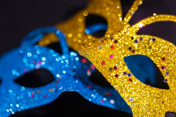 Yellow and blue shiny venetian carnival mask isolated on black background. New Year's party, hide...