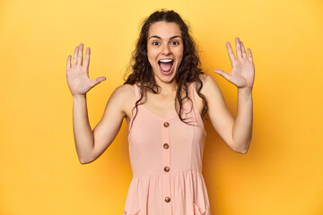 Young Caucasian woman, yellow studio background, receiving a pleasant surprise, excited and raising...
