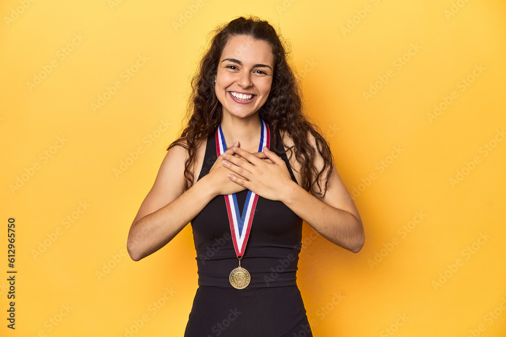 Wall mural happy young caucasian woman in sportswear with gold medal, yellow background.