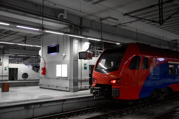 Red and blue passenger train at the platform of railway station. Commuter train is ready to departure from railway station