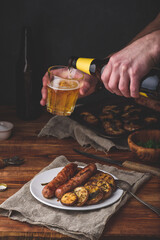 Pork sausages baked with eggplant, leek and herbs on white plate. Man Pouring Beer into a Glass.