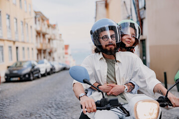 Happy tourist couple in protective hats are riding on rental vintage scooter in the Lisbon street © Daria