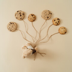 Teddy bear with chocolate cookies balloons on pastel cream background. Minimal sweet concept....