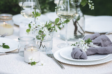 Romantic elegant luxury wedding table decor with white fresh spring blooming cherry apple tree flowers. Glass, candles, floral decoration for special marriage holiday event. No plastic zero waste