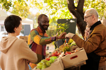 Elderly vendor giving apple sample to male customer, client trying out bio organic fresh fruits and...