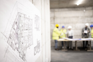 Blueprint at construction site and workers planning in background.