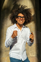 Stylish Urban Communication: Afro-Haired Guy in White Shirt and Glasses. City Charisma: Energetic Afro-Haired Guy Engaged in Phone Conversation. Dynamic Conversations: Afro Style in the Urban