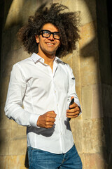 Fototapeta premium Stylish Urban Communication: Afro-Haired Guy in White Shirt and Glasses. City Charisma: Energetic Afro-Haired Guy Engaged in Phone Conversation. Dynamic Conversations: Afro Style in the Urban