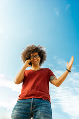 Afro-Styled Man Engrossed in an Energetic Phone Conversation. Charming Afro Guy Expressing with Gusto as he Talks, Backdrop of a Breathtaking Sky. Afro-Textured Man Talking Animatedly on the Phone