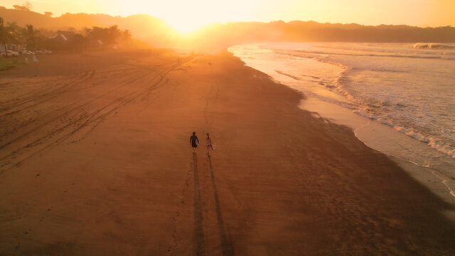 AERIAL: Stunning view of orange glowing sandy beach and rolling ocean waves